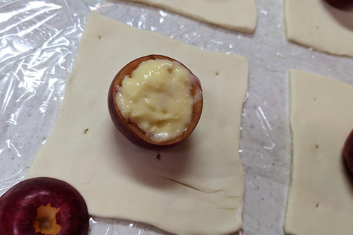 6. オーブンを190℃に温めておく。<br>中をくり抜いたりんごにカスタードクリームを詰め、切りとった上部を重ねてフタをし、正方形に切ったパイ生地の中央におく。