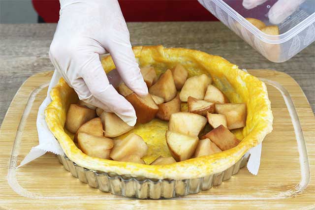 7.オーブンを200℃に予熱しておく。<br>一晩りんごジュースに漬けておいたりんごの水分をペーパータオルで拭き取り、焼けたパイ生地の上にのせる。